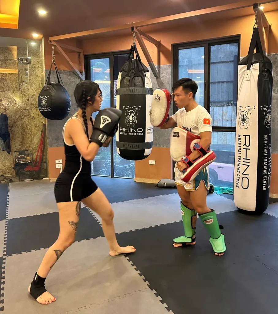 Muay Thai classes for women at RHINO Tay Ho, a student doing pad work with a coach