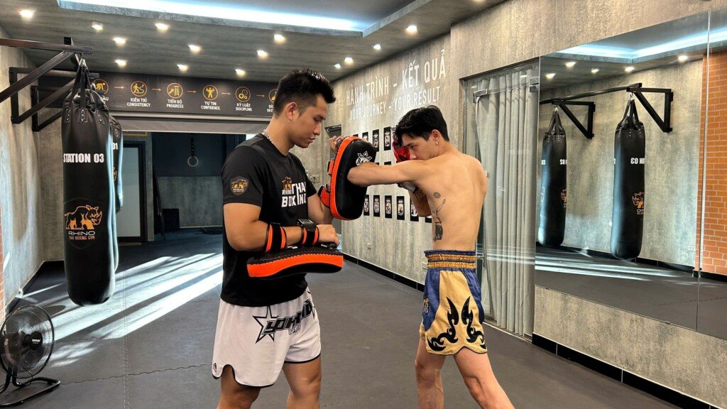 Heavy bag training benefits compared with pad work — a RHINO coach holds the pad for a student during a Muay Thai session in Tay Ho